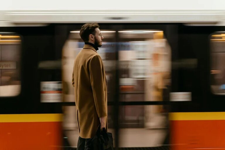 A Man in Brown Coat Standing on a Train Station Near a Moving Train