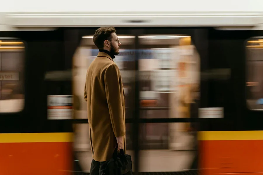 A Man in Brown Coat Standing on a Train Station Near a Moving Train