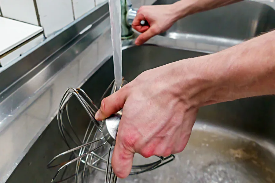 Người đàn ông đang rửa máy đánh trứng điện đã được tháo rời trong bồn rửa