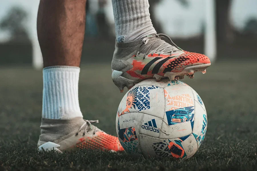 Hình ảnh cận cảnh của cầu thủ bóng đá mang giày Adidas, cầm bóng đá thương hiệu trên cỏ