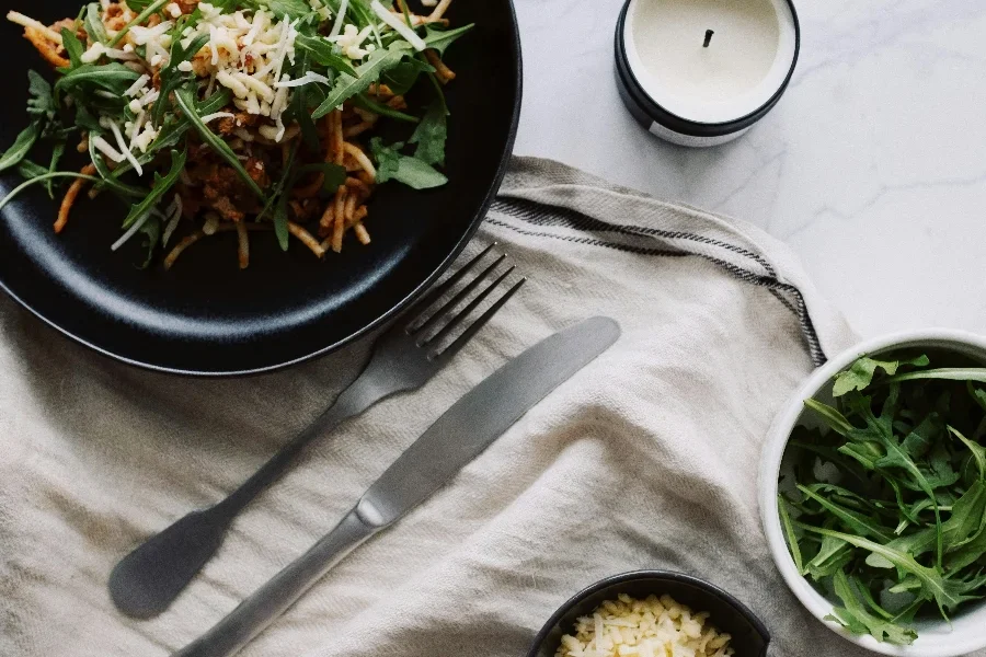 Món salad tươi được phục vụ trên đĩa đen với dĩa và dao đặt trên khăn trắng