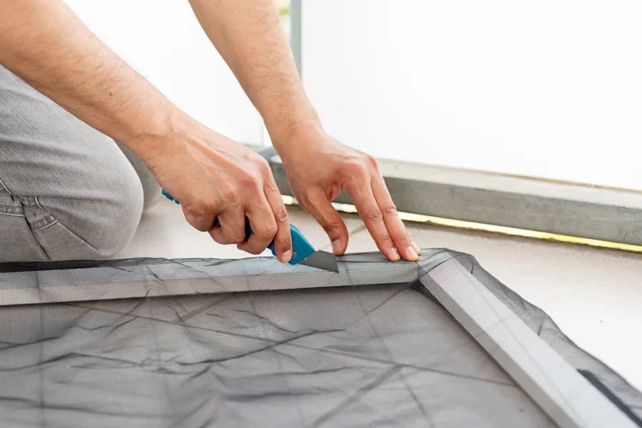 Người đàn ông đang sử dụng dao tiện ích để cắt lưới trên khung cửa sổ